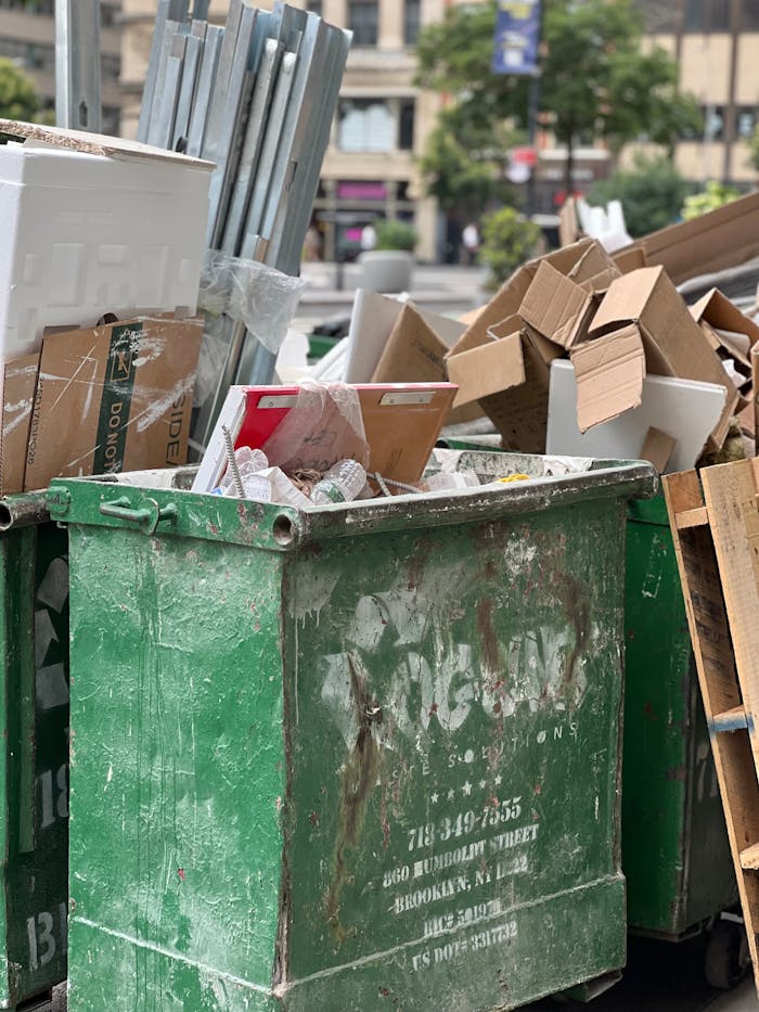 Overflowing dumpster with cardboard and various waste in urban setting.